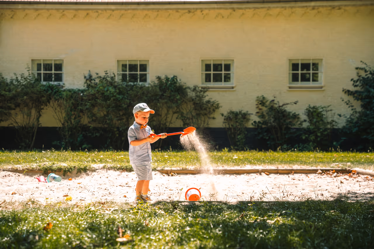 Een kleine jongen speelt in de zandbak met een oranje schep.